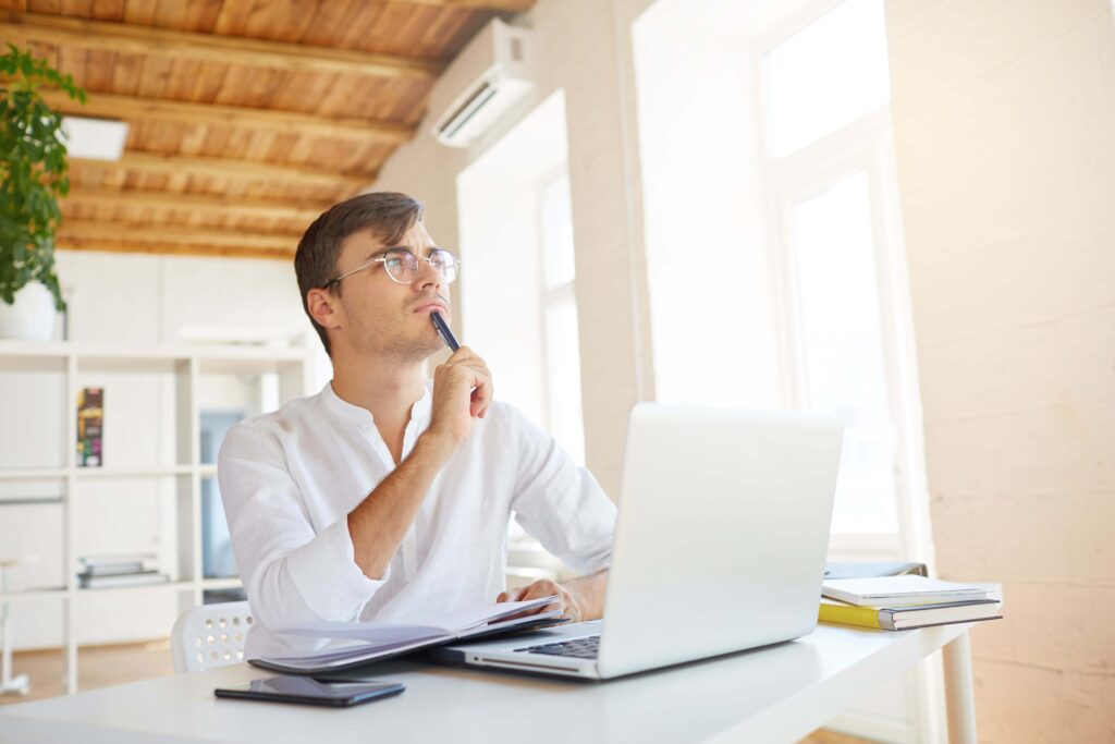 Young man writing on his computer, thinking about which English punctuation mark he should use.