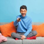 people-leisure-pastime-concept-overjoyed-unshaven-adult-man-sits-lotus-poses-sofa-holds-remote-control-watches-funny-show-television-min-150x150.jpg