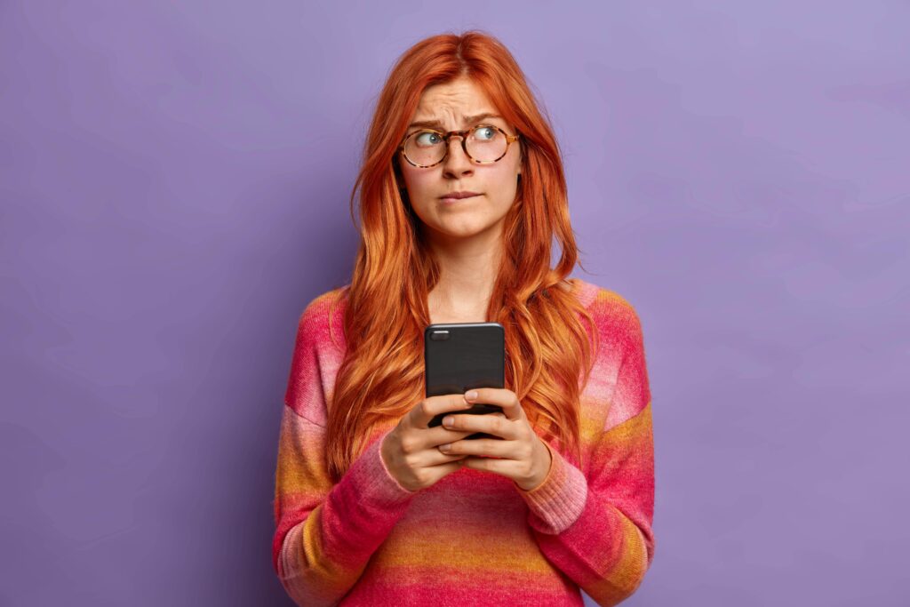 Red haired woman writing a work email on her cell phone, not sure about which English punctuation to use: an en dash or an em dash.