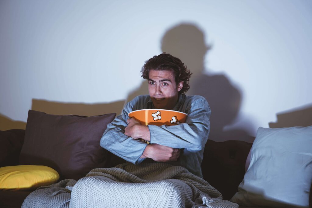 Young man hugging a huge bowl of popcorn because he's scared of Korean zombie movies.